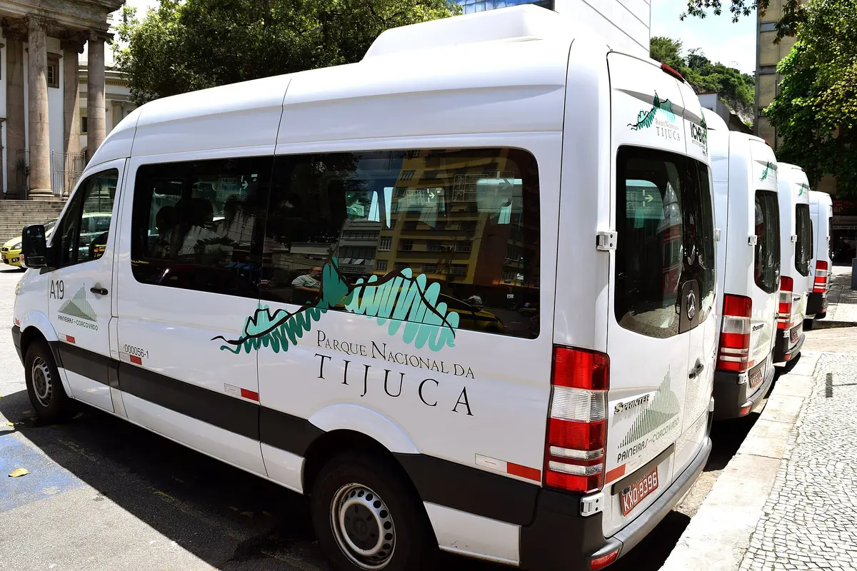 A row of white Paineiras-Corcovado minivans with Tijuca National Park branding parked at a kerb